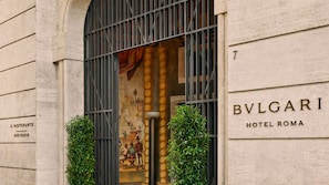 The exterior of BVLGARI Hotel Roma, featuring a classical facade with a large arched window, a mural, and the hotel's name prominently displayed.