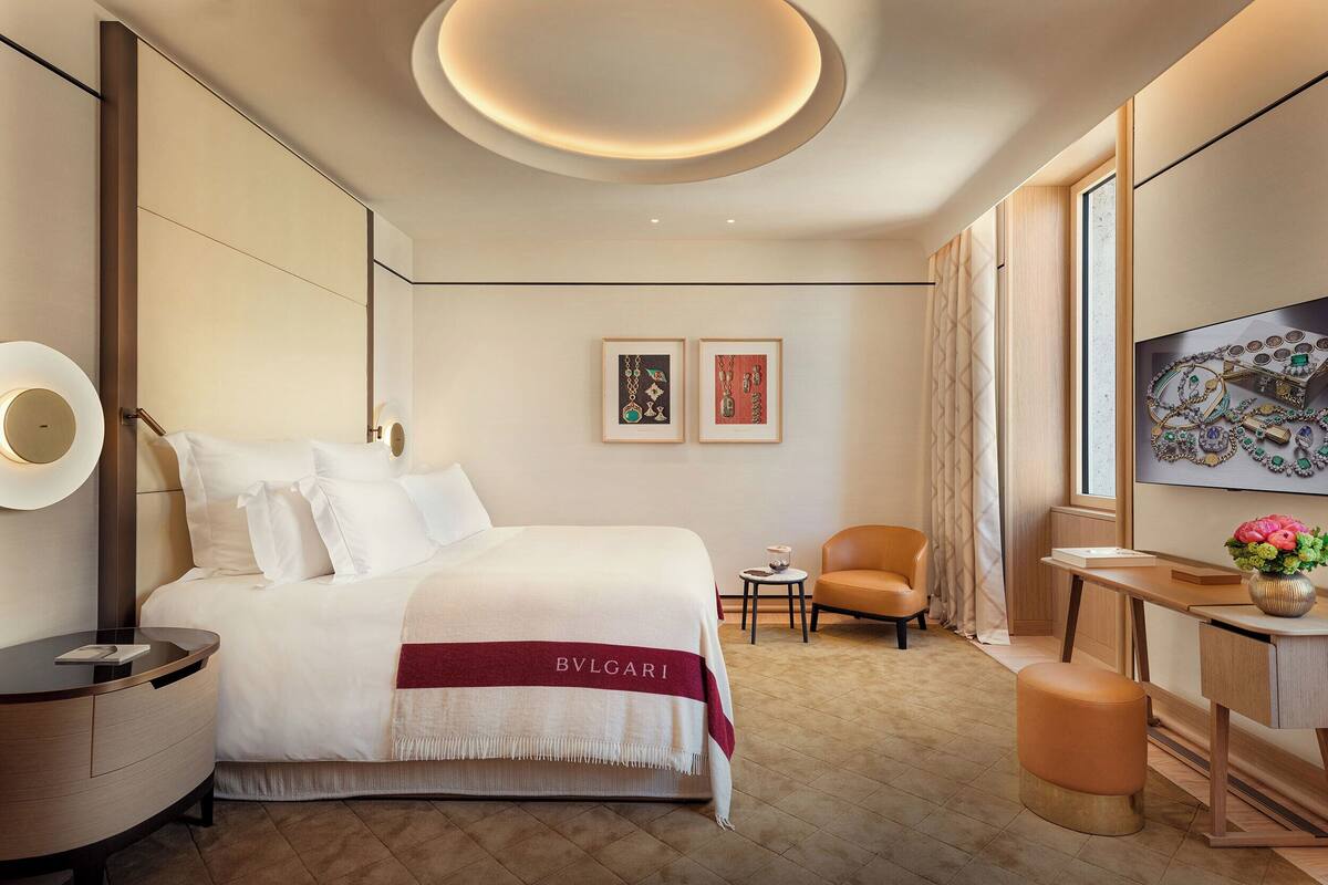 A hotel room with a large bed, a desk, a chair, and artwork on the wall.