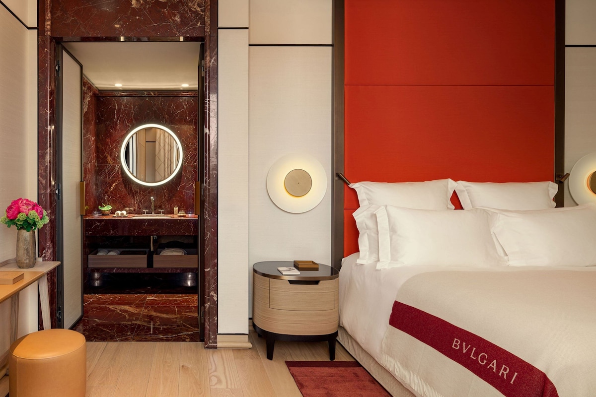 A modern bedroom with a large bed, a round mirror, a nightstand, and a vanity with a mirror.
