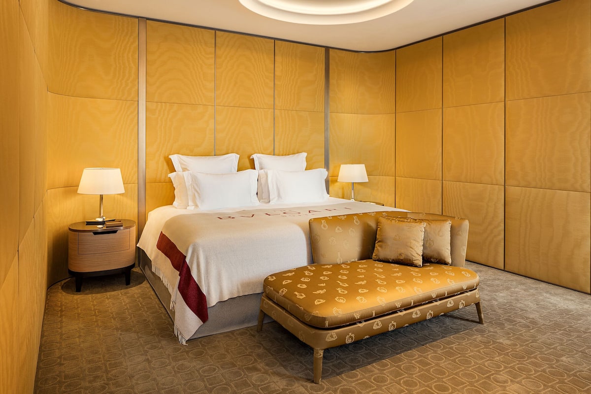 A hotel room with a large bed, two bedside tables, a sofa, and a patterned carpet.