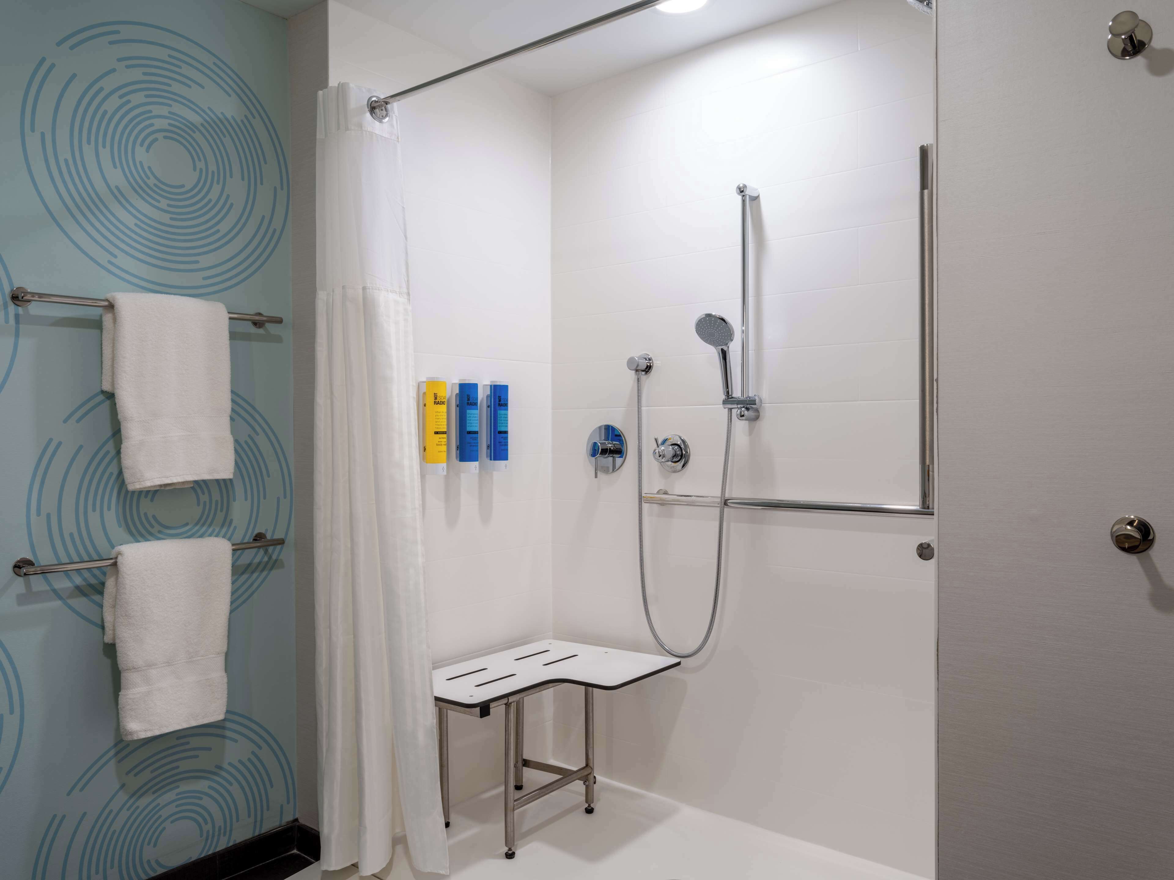 A modern shower area with a handheld showerhead, a glass-enclosed bench, and a towel rack with white towels.