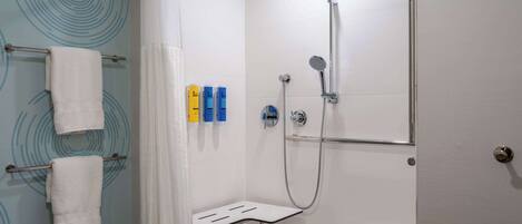 A modern shower area with a handheld showerhead, a glass-enclosed bench, and a towel rack with white towels.