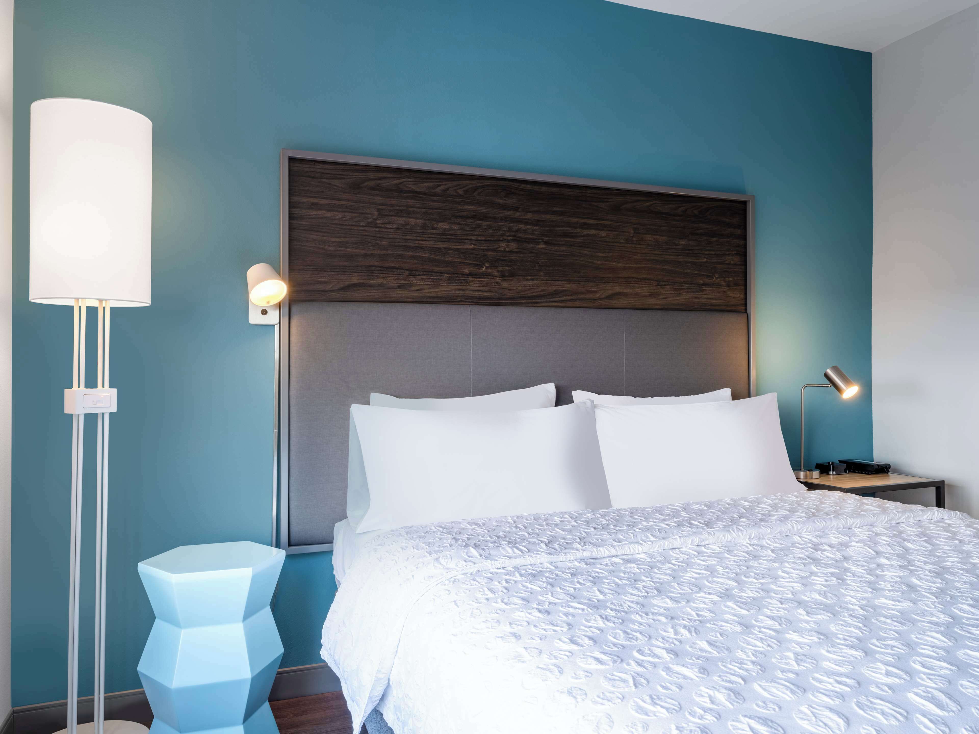 Un dormitorio moderno con una cama grande, una mesita de noche, una lámpara y un aplique de pared.