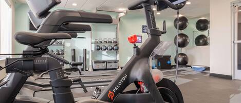 A stationary bike with a digital display, a wall-mounted TV, and exercise equipment in the background.
