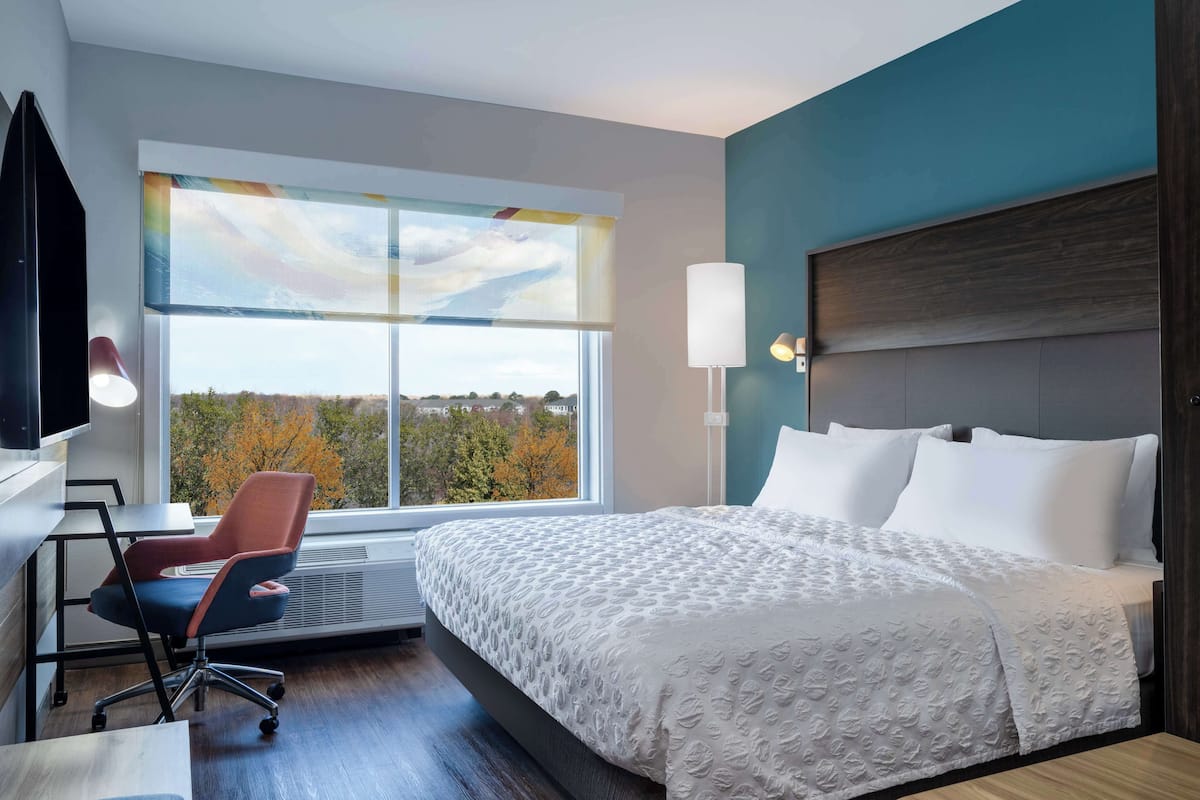 Une chambre d’hôtel avec un grand lit, un bureau avec une chaise, une télévision et une fenêtre donnant sur la verdure.