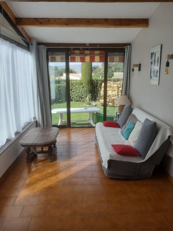 Ein Wohnzimmer mit einer Couch, einem Holztisch und Blick auf einen Garten durch große Fenster.