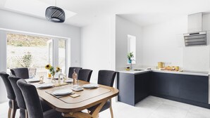 Uma cozinha moderna com uma ilha central, uma área de refeições com mesa e cadeiras de madeira, e uma janela grande que permite entrada de luz natural.