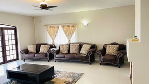Un salon avec trois canapés en cuir marron, une table basse en verre et un ventilateur de plafond.