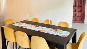 Un coin repas avec une table rectangulaire, six chaises jaunes, une nappe noire et un tableau représentant un coucher de soleil accroché au mur.