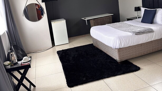 Ein modernes Schlafzimmer mit Bett, schwarzem Teppich, Schreibtisch, Stuhl, Spiegel und Deckenventilator.