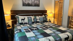 Een slaapkamer met een groot bed, twee bedlampen, een hoofdbord, een ingelijst beeld aan de muur, en een houten deur.