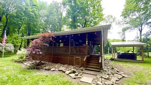 Een houten chalet met een overdekte veranda, een pad van stenen en een barbecueplek.