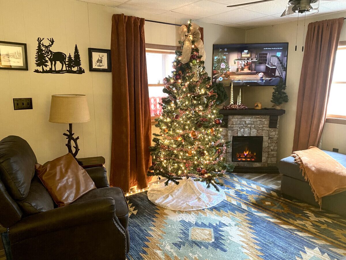 Un salon chaleureux avec un sapin de Noël, un fauteuil en cuir, une cheminée et un téléviseur.