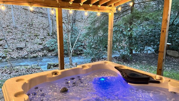 A hot tub with a wooden pergola overhead, surrounded by a forested area.