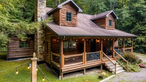 A log cabin with a stone chimney, a porch with outdoor seating, and a stone staircase leading to the entrance.