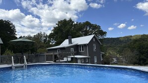 Una piscina con terraza de madera y una casa al fondo.