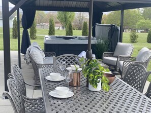An outdoor patio with a covered seating area, a hot tub, and a table set for dining.