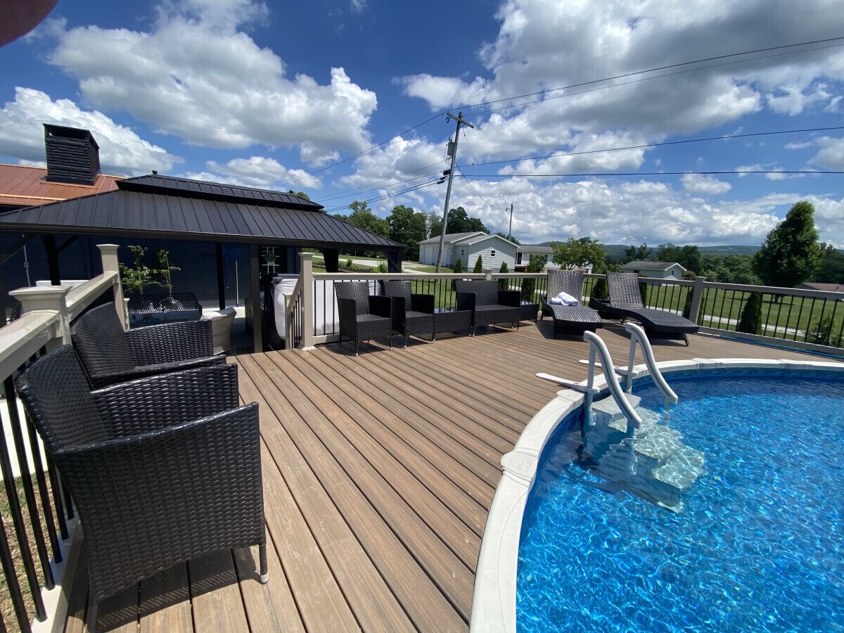 A wooden deck with a swimming pool, outdoor furniture, and a covered area with a metal roof.