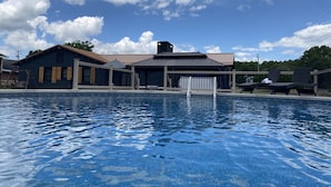 Une piscine dotée de chaises longues et d’un espace abrité, le tout entouré d’un bâtiment dont le toit est en métal.