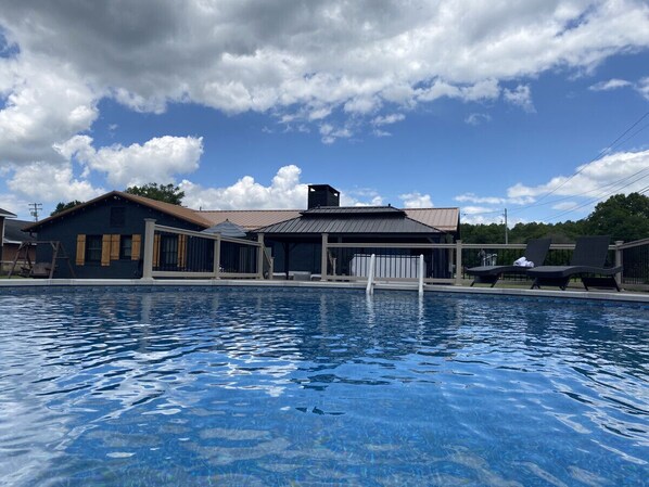 A swimming pool with lounge chairs and a covered area, surrounded by a building with a metal roof.