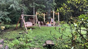 Puisesta valmistettu keinuteline, nuotiopaikka ja oleskelualue metsäisessä ulkotilassa.