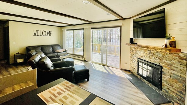 A modern living room with a fireplace, a black leather sofa, and a 'WELCOME' sign on the wall. - Castle Rock Lakefront Home, with pier, sand bottom, and wrap around deck (Arkdale)