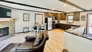 A modern kitchen with wooden cabinets, a refrigerator, and a microwave. There is a dining area with a table and chairs. - Castle Rock Lakefront Home, with pier, sand bottom, and wrap around deck (Arkdale)