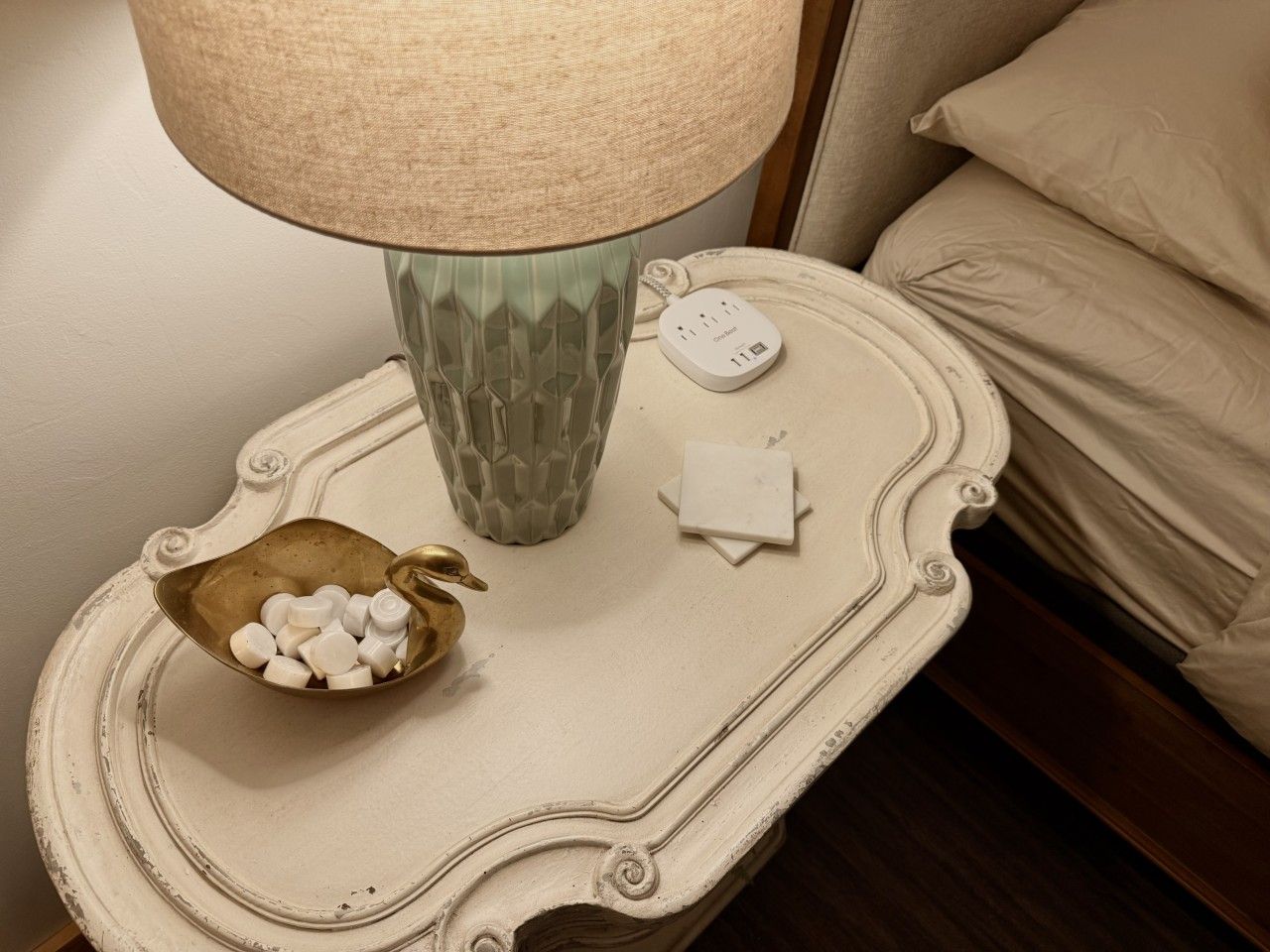 A bedside table with a lamp, a decorative bowl, and a power adapter.