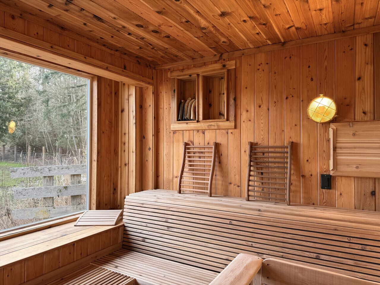 A wooden sauna with benches, a window, and a wall-mounted light fixture.