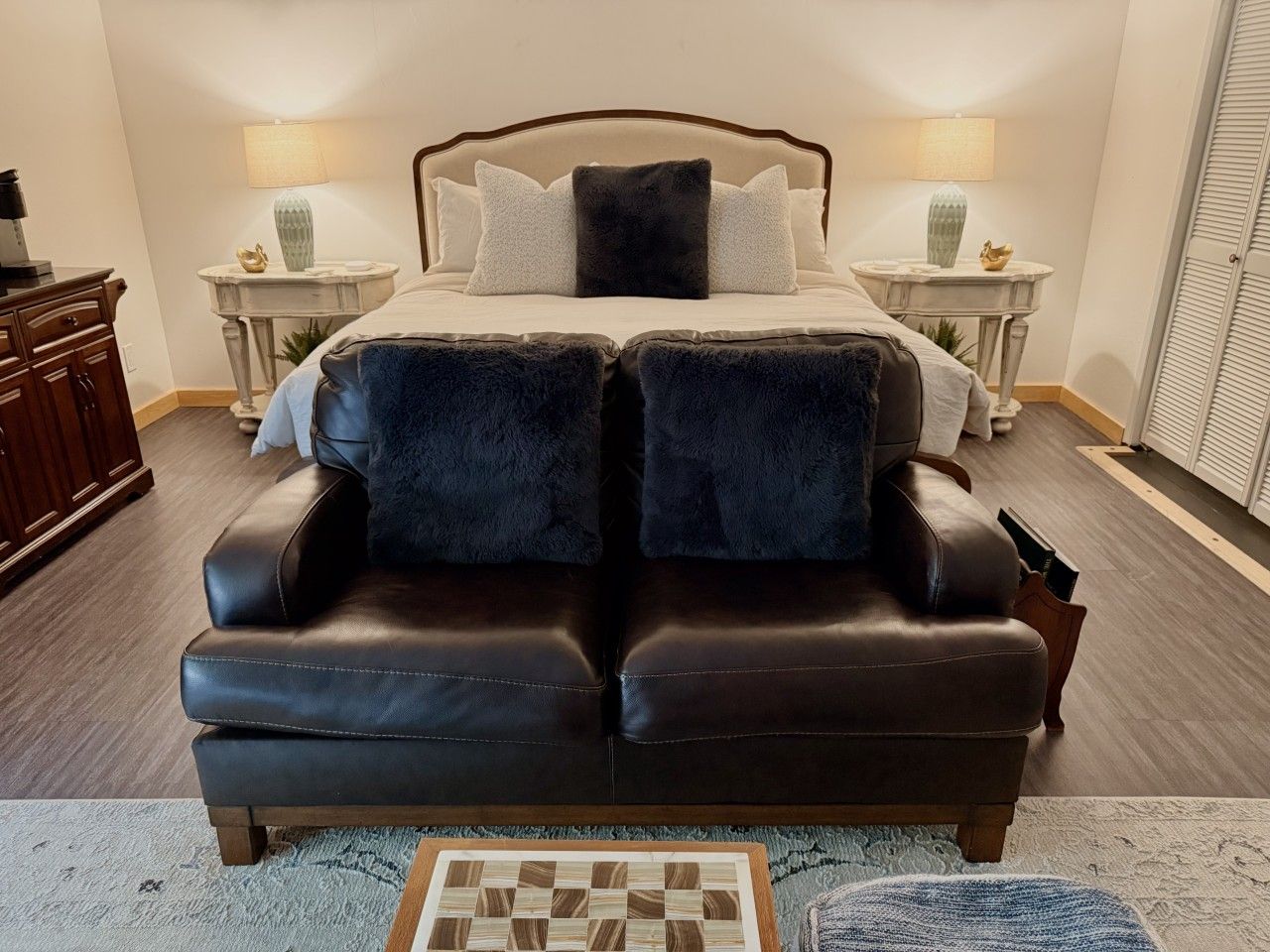Une chambre avec un grand lit, deux tables de chevet avec des lampes, un canapé en cuir foncé et un petit tapis.