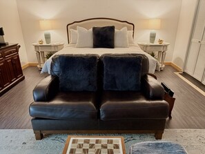 A bedroom with a large bed, two bedside tables with lamps, a dark leather sofa, and a small rug. - Romantic PentHaus Suite - Hot Tub & Sauna (Port Angeles)