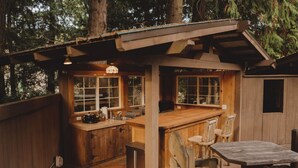 A wooden cabin with a kitchen and dining area, surrounded by trees. - Romantic PentHaus Suite - Hot Tub & Sauna (Port Angeles)