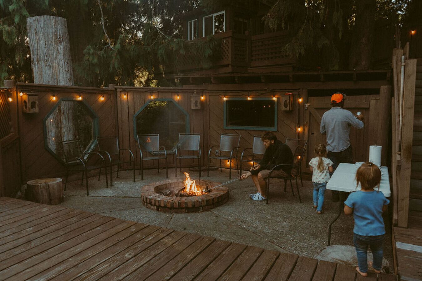 An outdoor seating area with a fire pit, wooden deck, and string lights.