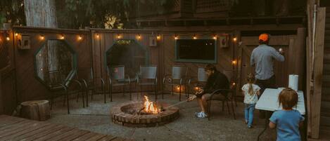 An outdoor seating area with a fire pit, wooden deck, and string lights.