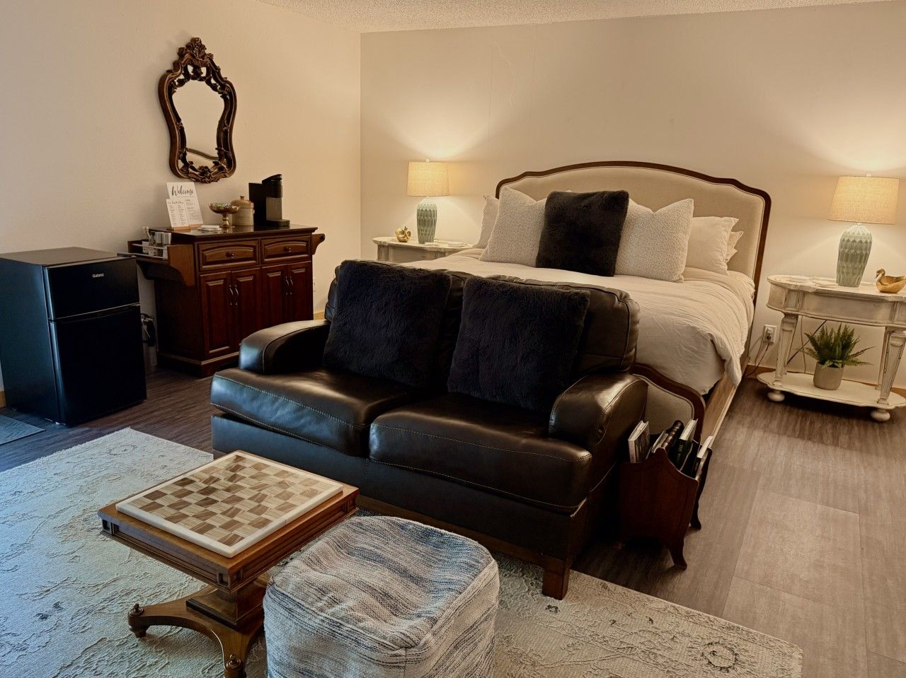 A bedroom with a bed, a leather sofa, a small table, and a nightstand with lamps.