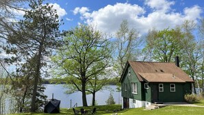 A green house with a brown roof by a lake, surrounded by trees and a grassy lawn. - Classic MN Up North Lake House w/Sauna (Aitkin)