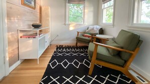 A cozy room with a wooden bookshelf, a green armchair, a small round table, and a patterned rug. - Classic MN Up North Lake House w/Sauna (Aitkin)
