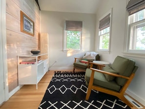 A cozy room with a wooden bookshelf, a green armchair, a small round table, and a patterned rug. - Classic MN Up North Lake House w/Sauna (Aitkin)