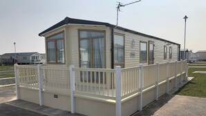 Une maison mobile dotée d’une véranda clôturée, de grandes fenêtres et d’une antenne parabolique.