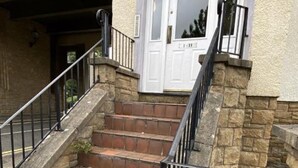 Steinelemente einer Treppe führen zu einer weißen Tür mit einem schwarzen Metallgeländer.