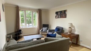 Ein Wohnzimmer mit einer Couch, zwei Sesseln, einem Couchtisch, einem TV-Schrank und einer Lampe.