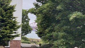 Ein rotes Auto auf einer Auffahrt vor einem weißen Gebäude und einer Brücke im Hintergrund.