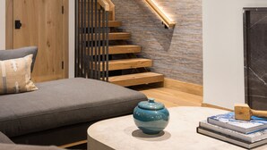 A modern living room with a wooden staircase, a sofa, a coffee table, and a TV mounted on the wall. - Newly remodeled 4 bedroom condo only 1 block to Bridge St. & ski slopes, fre (Vail)