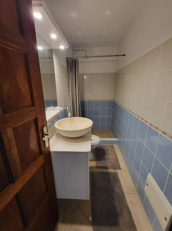 A bathroom with a wooden door, a white sink, a mirror, and blue-tiled walls.