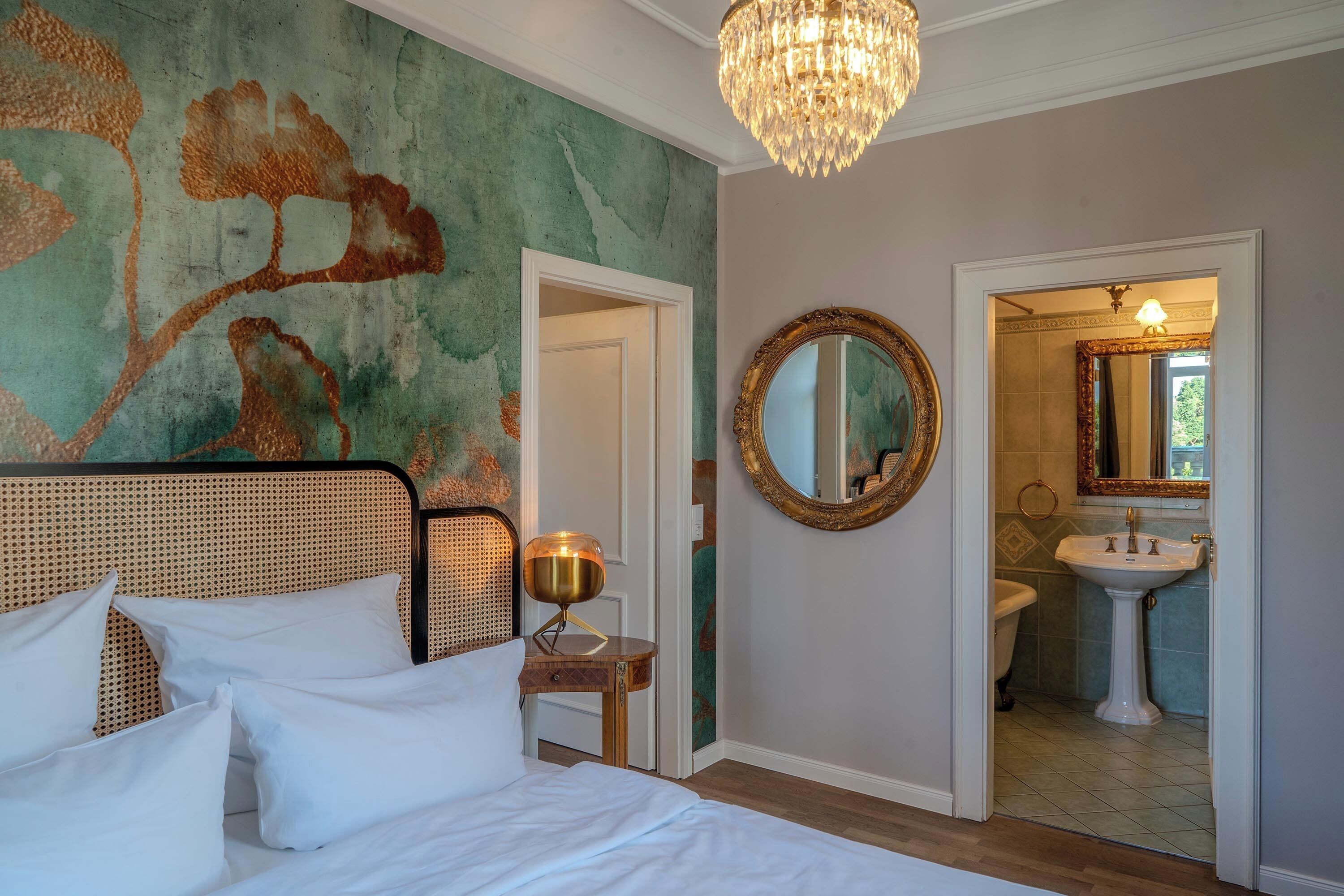 A bedroom with a bed, a bedside table, a lamp, a mirror, and a view into the bathroom.
