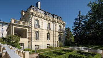 A large, classical building with multiple balconies and a formal garden with a fountain.