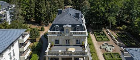 A large, historic building with a symmetrical facade, a central entrance, and a formal garden with a fountain.