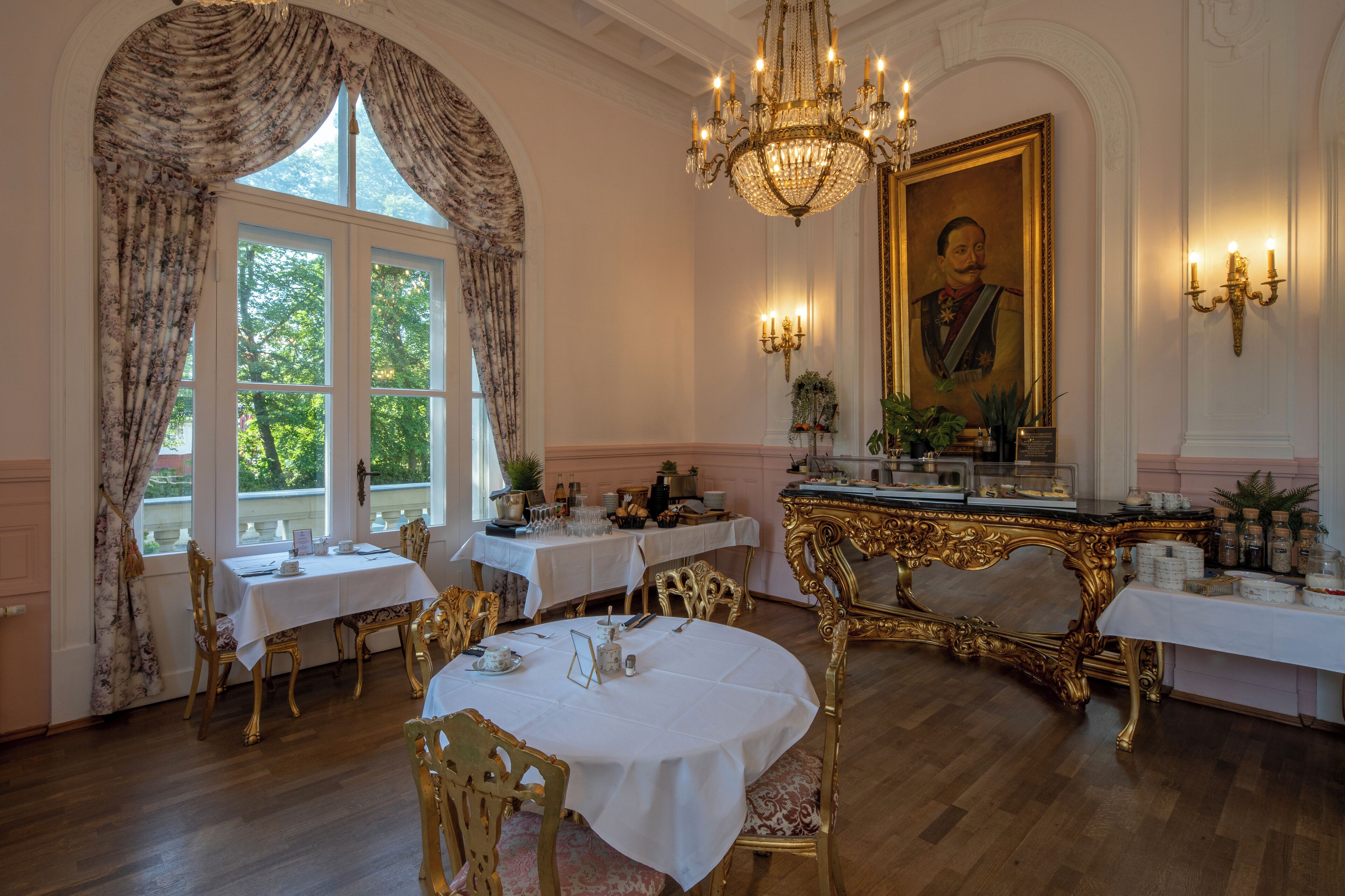 A formal dining room with ornate gold chairs, white tables, and a chandelier.