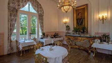 A formal dining room with ornate gold chairs, white tables, and a chandelier.