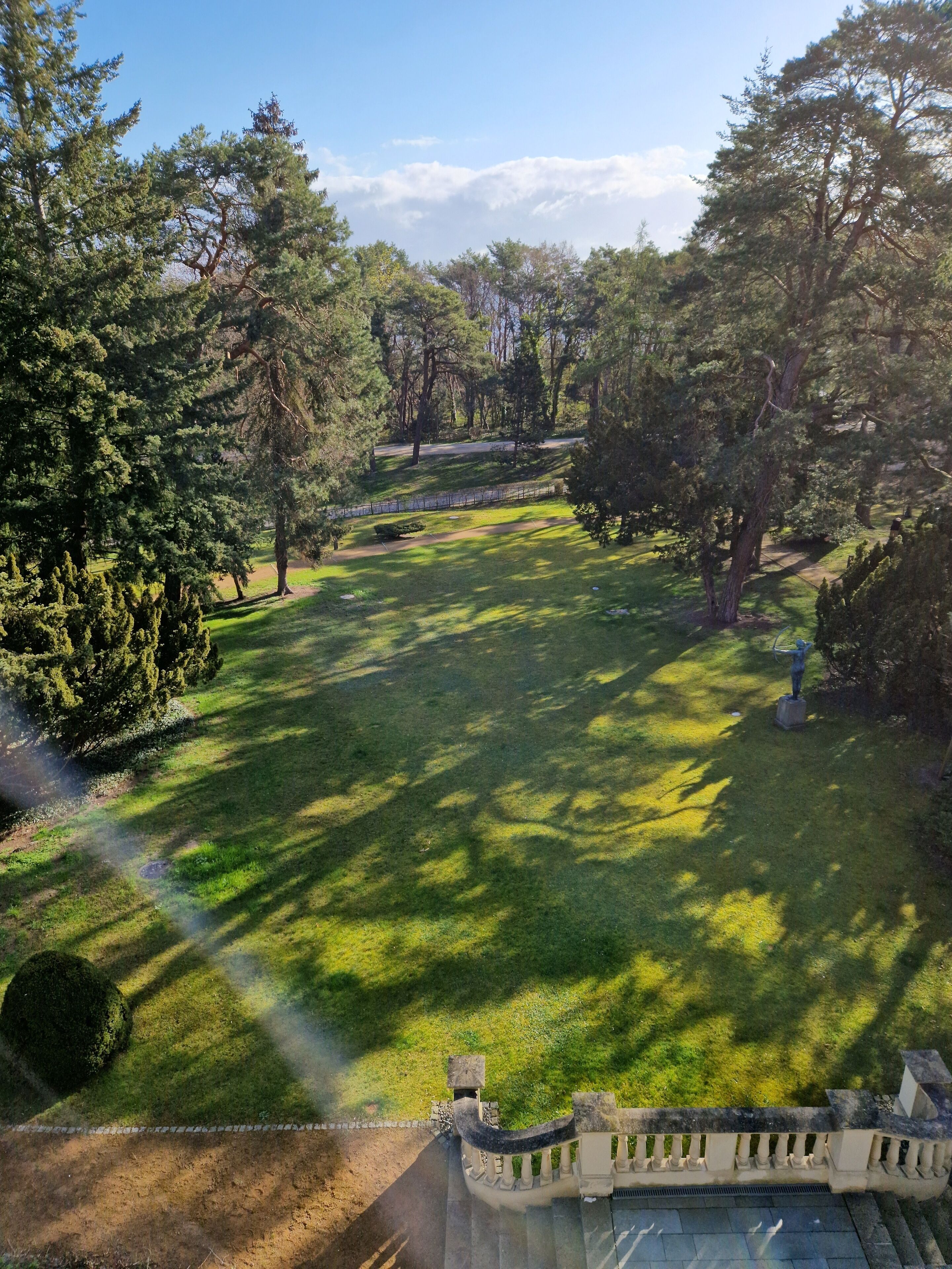 Un parque con balaustrada de piedra, árboles y cielo despejado.